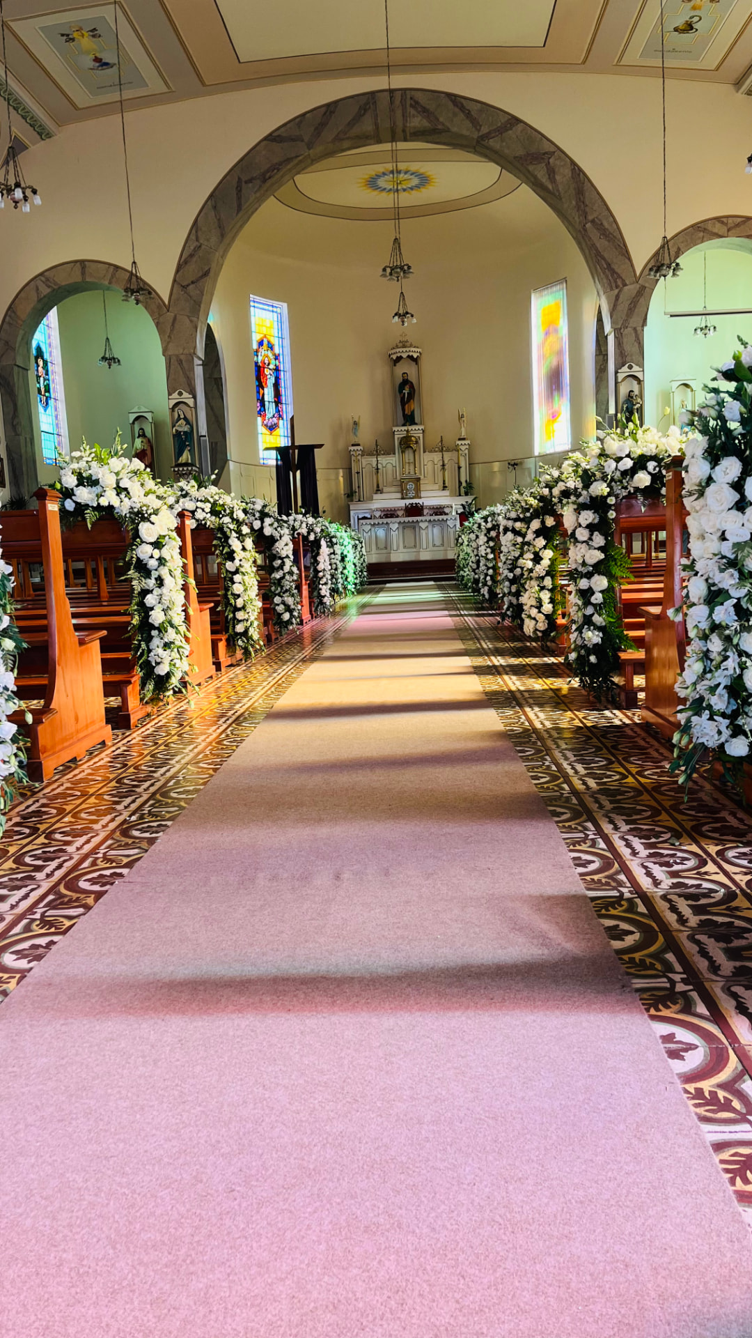 Igreja decorada com arcos de flores brancas e passadeira no corredor