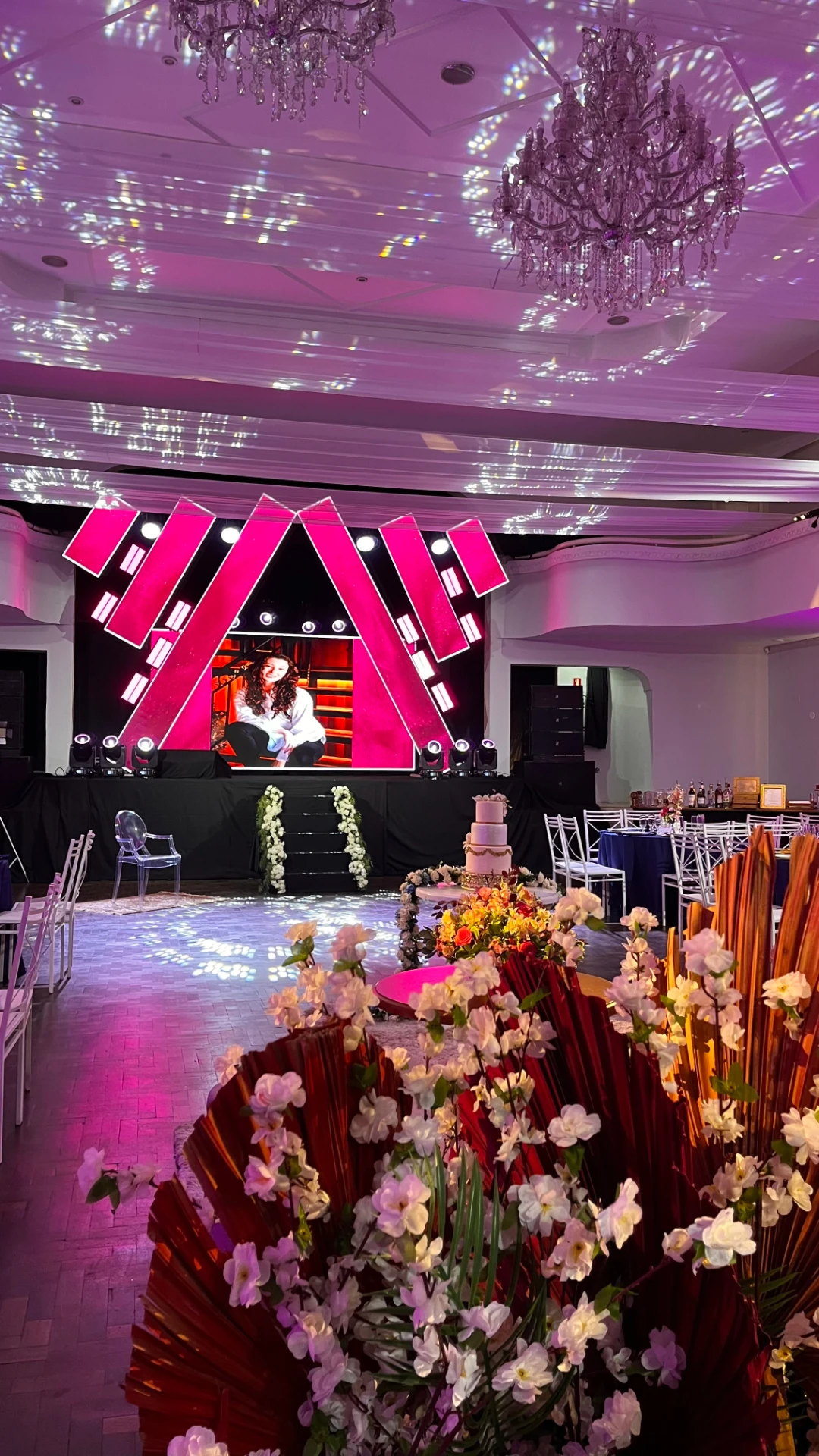 Palco e pista de dança iluminados em rosa com bolo e arranjos florais