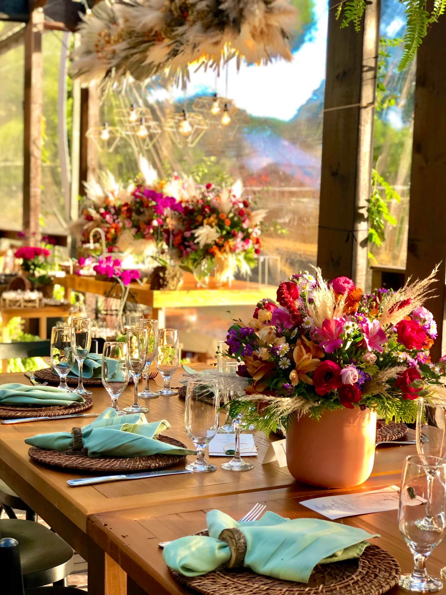 Mesa de jantar corporativo com arranjo floral colorido, pampas e vista para a natureza