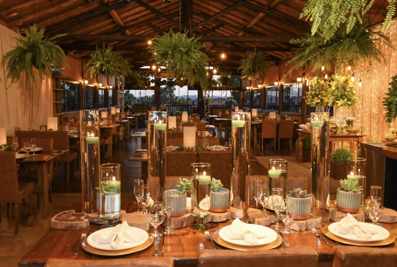 Salão de casamento rústico com samambaias suspensas, velas e cortina de luzes